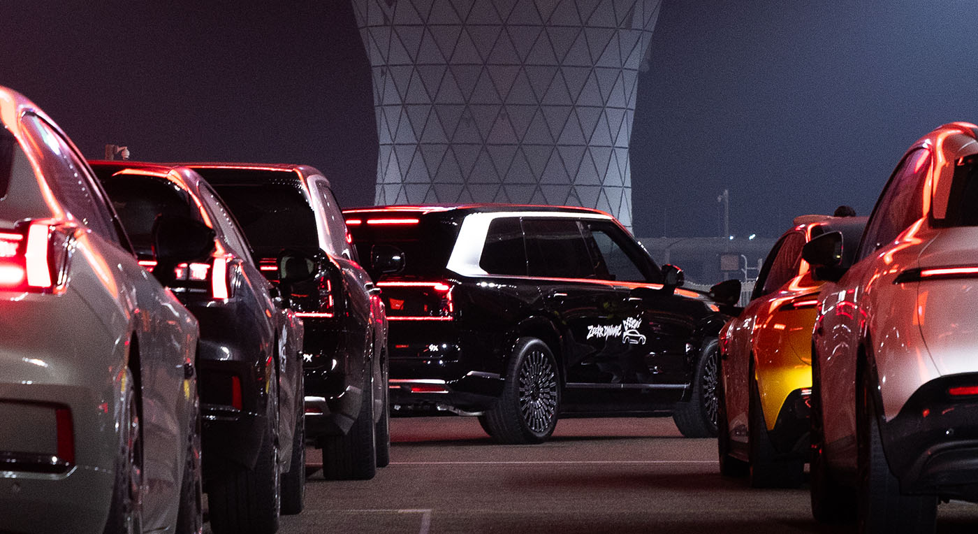 Rear view of a lineup of electric cars with glowing red LED taillights parked on a race track at night.